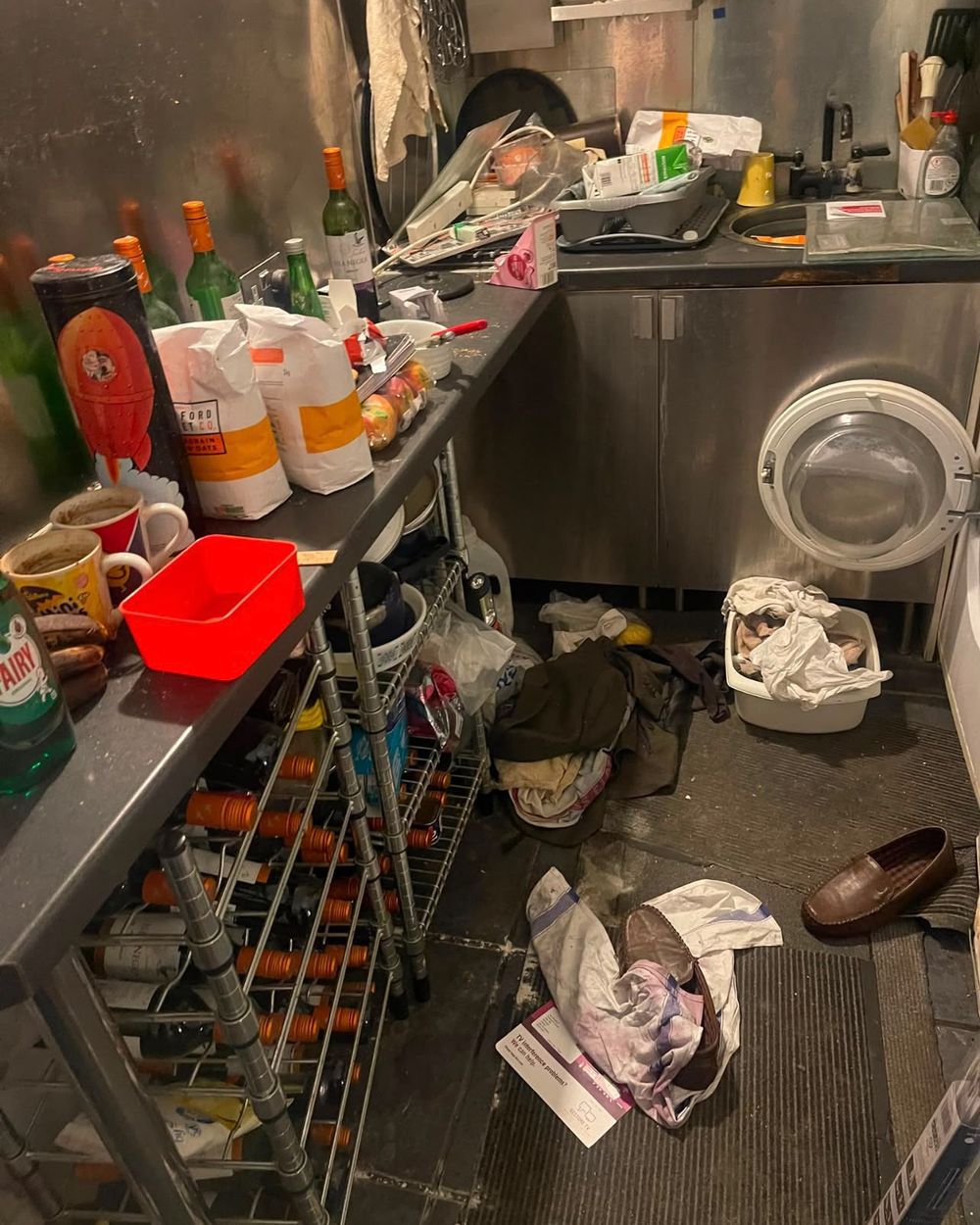 Kitchen before cleaning: worktops covered in bottles, food and rubbish, clothes on the floor